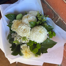 A bouquet of white and cream flowers with green foliage, wrapped in white tissue paper 